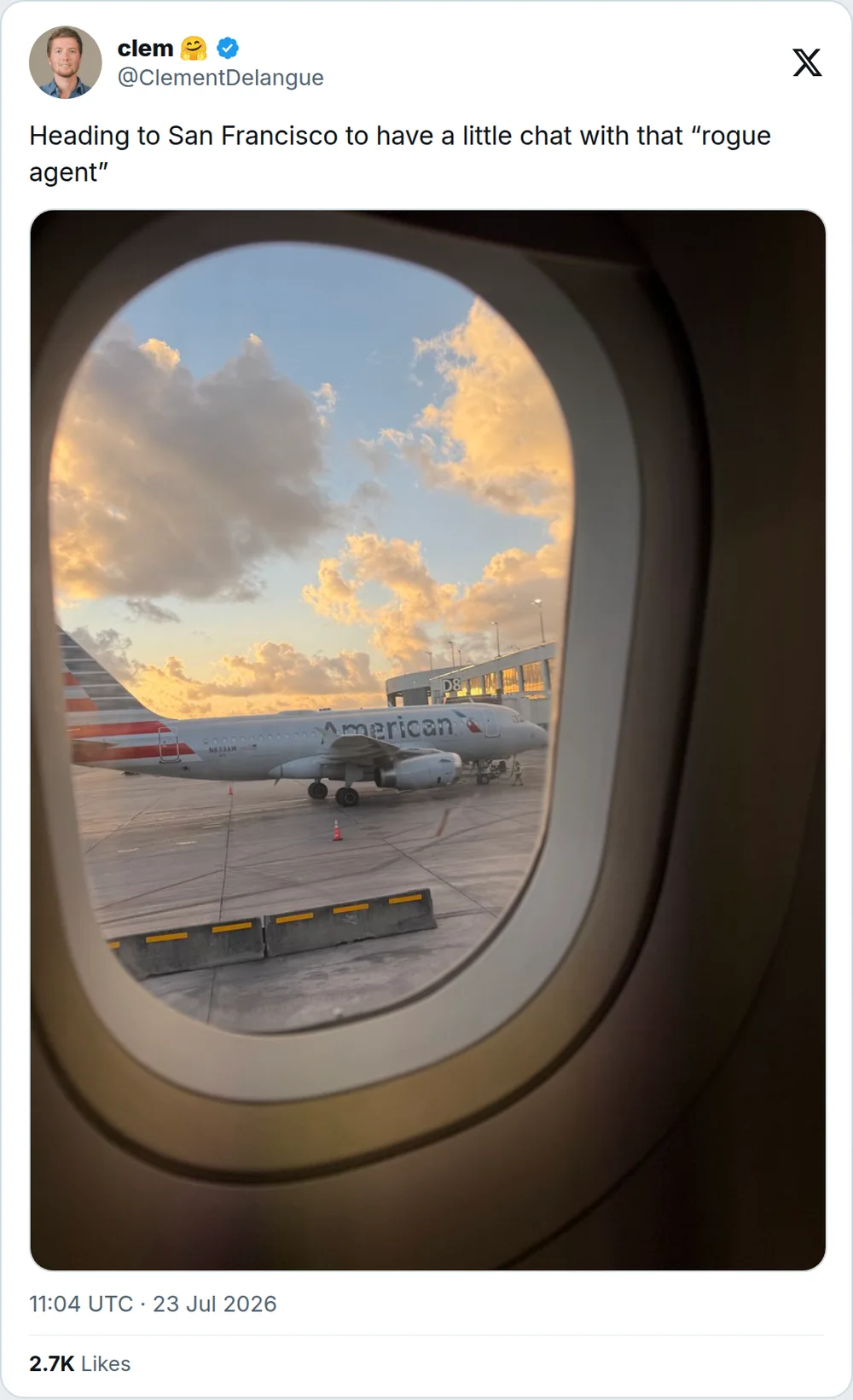 Delangue’s post on X, 23 July 2026: a photograph through a plane window at the gate, captioned “Heading to San Francisco to have a little chat with that ‘rogue agent’”.