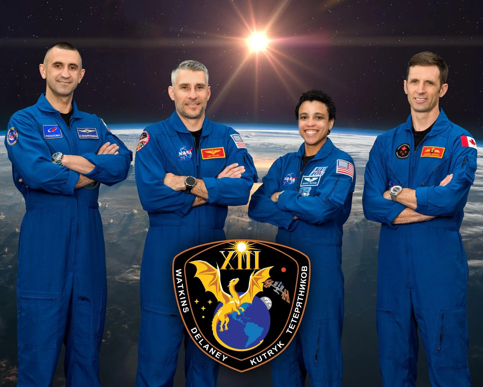 Official Crew-13 portrait of four crew in blue flight suits with arms folded in front of an image of Earth from orbit and a bright sun, from left Sergey Teteryatnikov, Luke Delaney, Jessica Watkins and Joshua Kutryk, above the black Crew-13 mission patch showing a gold dragon over Earth, the Roman numeral XIII and the four surnames