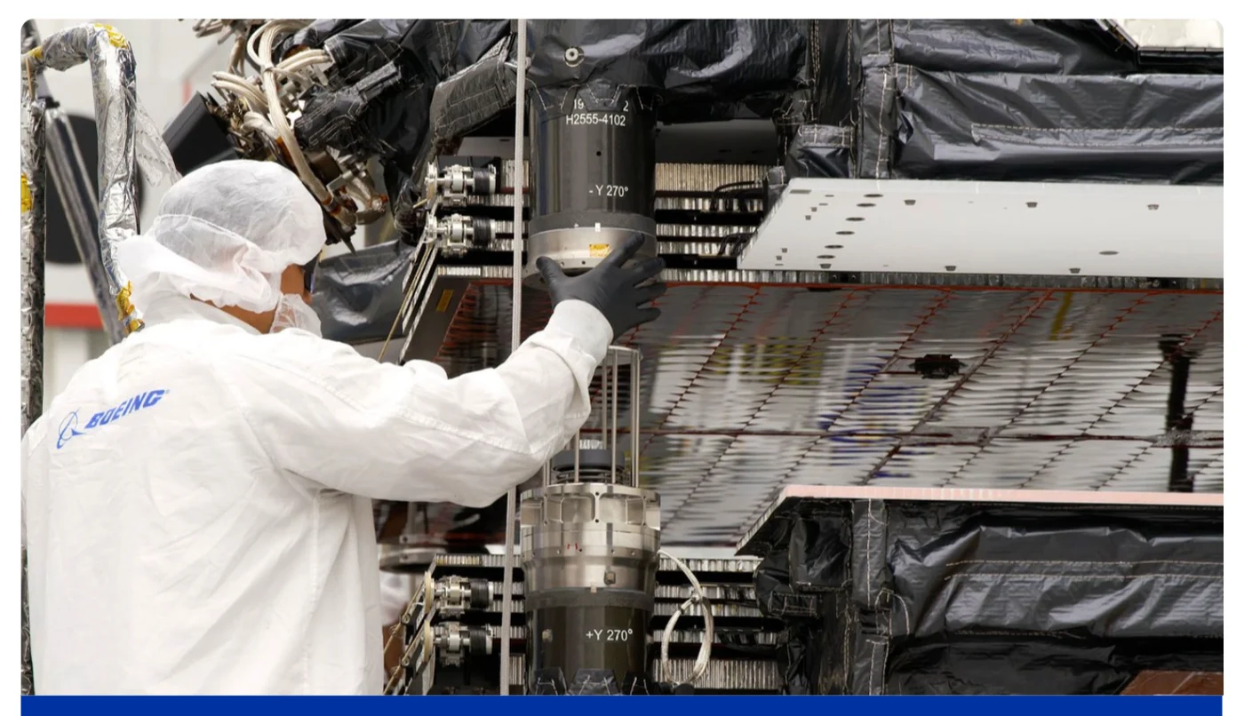 A Boeing technician in cleanroom clothing works beside an O3b mPOWER spacecraft.