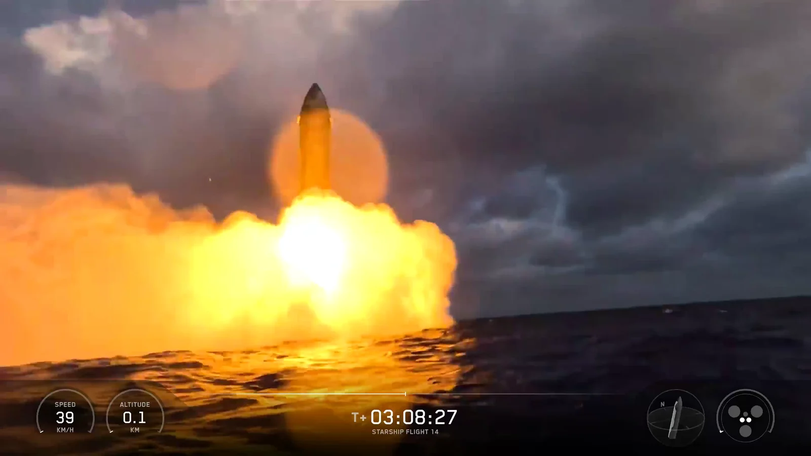 Frame from SpaceX's Flight 14 video, taken from a camera at sea level 3 hours 8 minutes 27 seconds after liftoff: the steel Starship stands upright a few metres above dark Pacific waves, its engines firing into a wide orange fireball of flame and steam, under heavy grey cloud. On-screen readouts give a speed of 39 km/h and an altitude of 0.1 km.