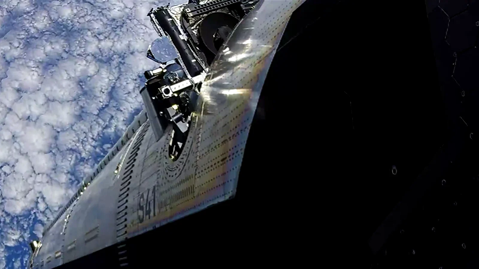 Frame from SpaceX's Flight 14 video 35 minutes 7 seconds after liftoff: a Starlink V3 satellite, a dark box of hardware with a round reflective panel, slides out of a slot high on the side of Starship's steel hull, which is marked S41, above a sea of small white clouds.