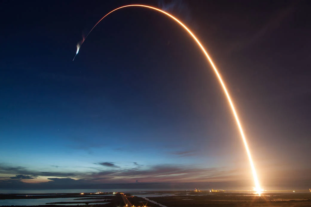 A Falcon 9 launch leaves a bright arc across the dawn sky.